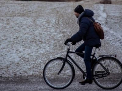 Jonge man met winterjas, sjaal en muts fietst over een onverharde weg