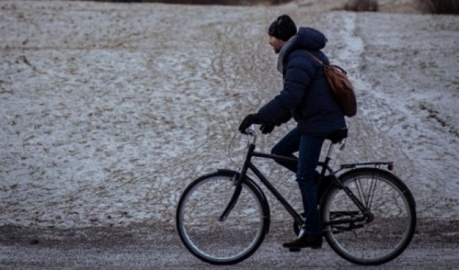 Jonge man met winterjas, sjaal en muts fietst over een onverharde weg